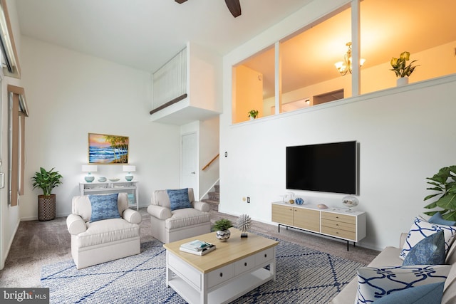 carpeted living room featuring ceiling fan with notable chandelier and a high ceiling