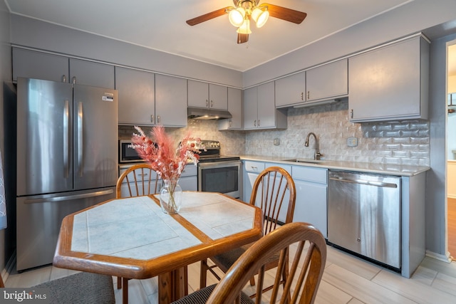 kitchen with appliances with stainless steel finishes, gray cabinets, sink, and backsplash