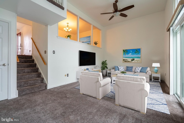 living room with a towering ceiling, ceiling fan with notable chandelier, and dark colored carpet