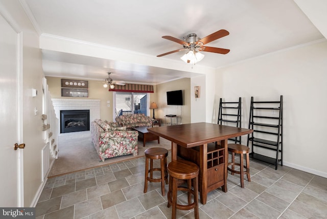 dining room with crown molding, ceiling fan, light carpet, and a brick fireplace