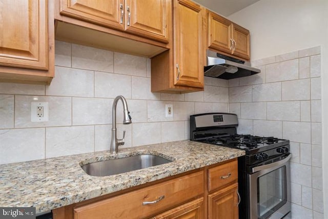 kitchen featuring stainless steel gas range oven, sink, backsplash, and light stone counters