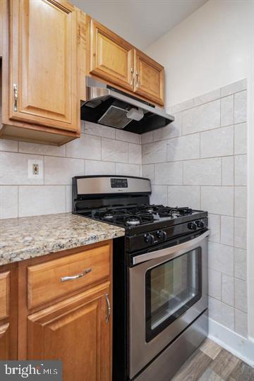 kitchen with light stone counters, stainless steel range with gas stovetop, tasteful backsplash, and hardwood / wood-style flooring