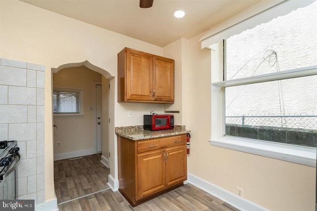 kitchen with stainless steel gas stove, ceiling fan, and light wood-type flooring