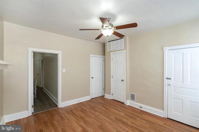 unfurnished bedroom featuring connected bathroom, two closets, wood-type flooring, and ceiling fan