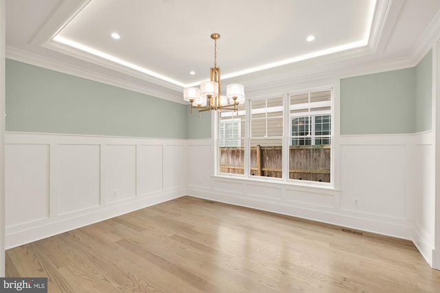 unfurnished dining area with a chandelier, light wood-type flooring, a raised ceiling, and wainscoting