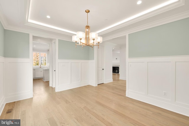 unfurnished dining area featuring a fireplace, visible vents, light wood-style floors, wainscoting, and an inviting chandelier