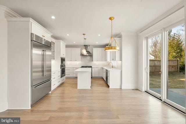 kitchen with tasteful backsplash, light wood-style floors, wall chimney exhaust hood, and built in appliances