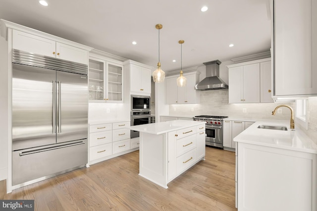 kitchen featuring wall chimney exhaust hood, a kitchen island, built in appliances, light wood-style floors, and a sink