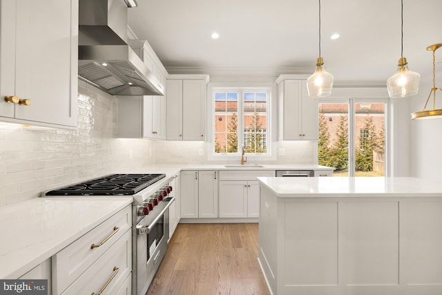 kitchen featuring white cabinets, wall chimney exhaust hood, appliances with stainless steel finishes, light countertops, and backsplash