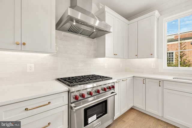 kitchen featuring wall chimney exhaust hood, white cabinetry, luxury range, and backsplash