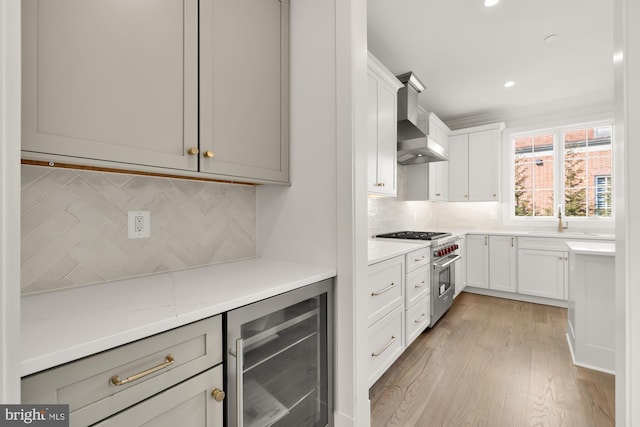 kitchen featuring wine cooler, a sink, wall chimney range hood, high end stainless steel range, and light wood finished floors