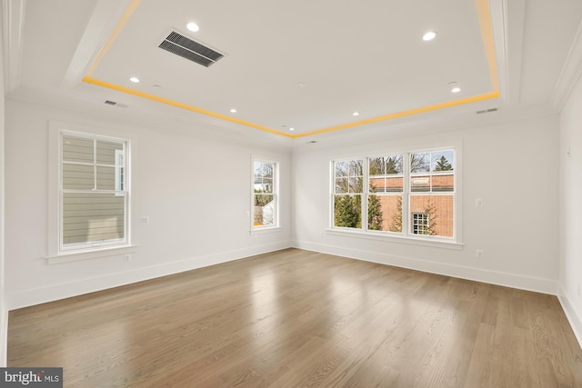 unfurnished room featuring a tray ceiling, visible vents, and wood finished floors