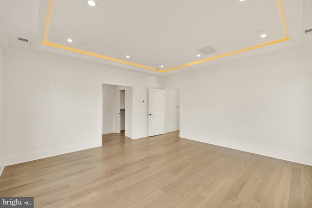 empty room with visible vents, baseboards, a tray ceiling, light wood finished floors, and crown molding