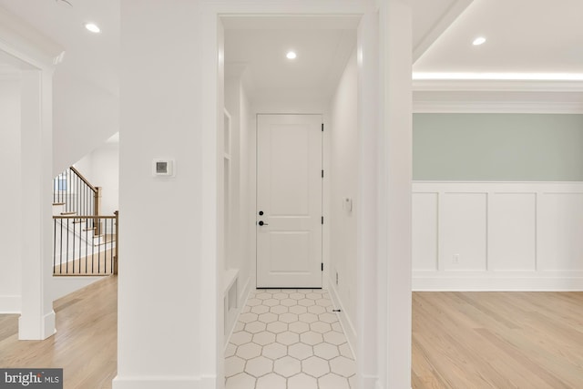 corridor featuring light wood-type flooring, stairs, a decorative wall, and recessed lighting