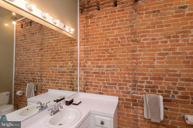 bathroom with vanity, toilet, and brick wall