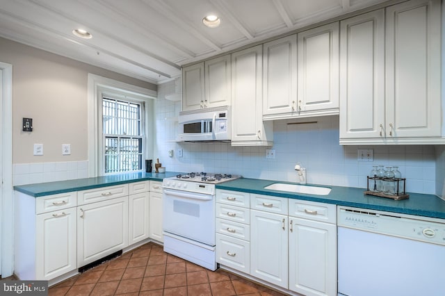 kitchen with tasteful backsplash, sink, white cabinets, dark tile patterned floors, and white appliances