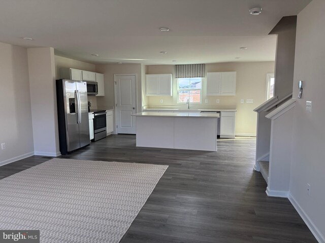 kitchen with a kitchen island, appliances with stainless steel finishes, white cabinetry, sink, and dark wood-type flooring