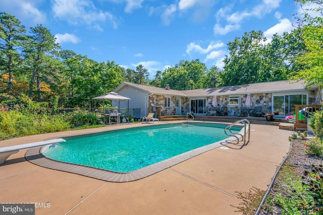 view of swimming pool with a grill, a diving board, and a patio area