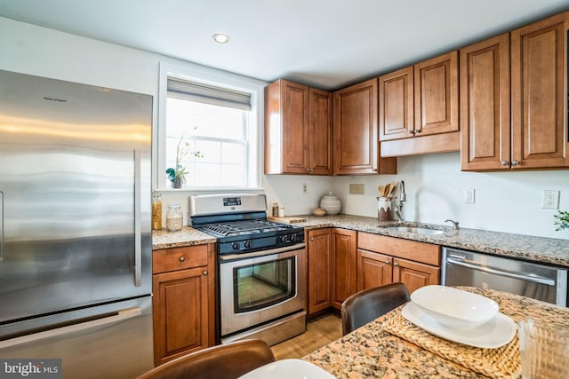 kitchen featuring brown cabinets, light stone counters, stainless steel appliances, and a sink