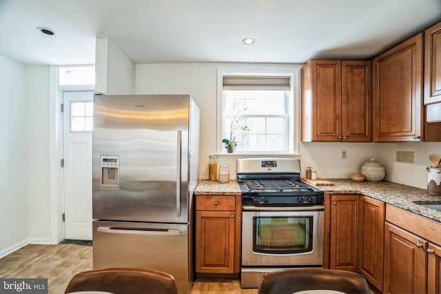 kitchen with appliances with stainless steel finishes, a healthy amount of sunlight, brown cabinets, and light stone countertops