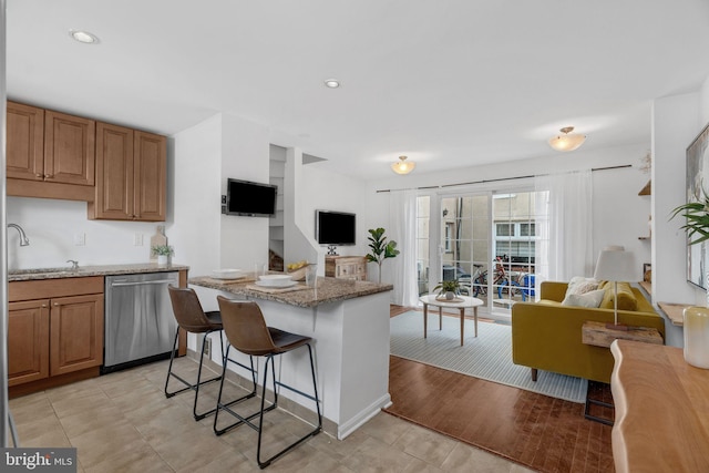 kitchen featuring brown cabinets, stainless steel dishwasher, open floor plan, light stone countertops, and a kitchen bar