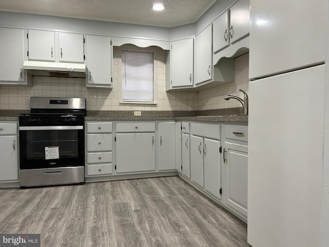 kitchen featuring white refrigerator, stainless steel range with gas stovetop, light hardwood / wood-style flooring, and white cabinets