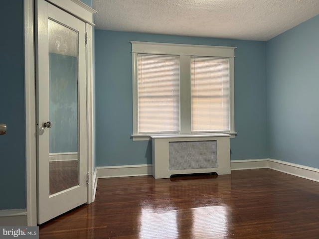 spare room with dark wood-type flooring, radiator heating unit, and a textured ceiling