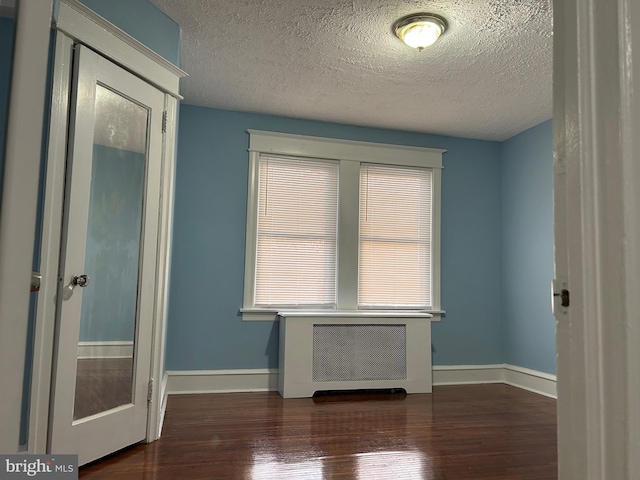 unfurnished room featuring dark hardwood / wood-style floors, radiator heating unit, and a textured ceiling