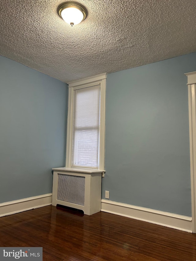 unfurnished room featuring dark hardwood / wood-style floors, radiator heating unit, and a textured ceiling