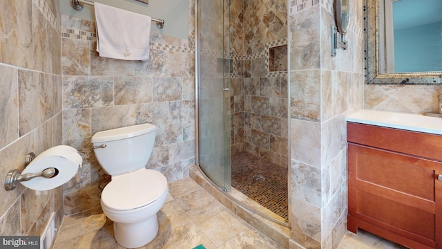 bathroom with tile walls, an enclosed shower, vanity, and toilet