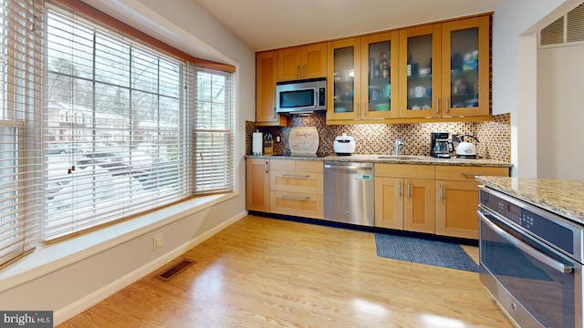 kitchen with light stone counters, stainless steel appliances, light hardwood / wood-style floors, and tasteful backsplash