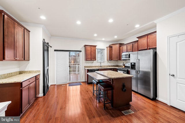 kitchen with a breakfast bar area, stainless steel appliances, light stone countertops, a kitchen island, and a barn door