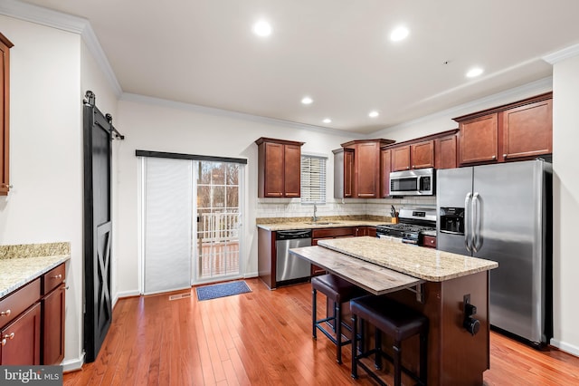 kitchen with light stone counters, stainless steel appliances, a barn door, and a kitchen island