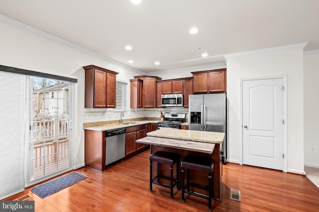 kitchen with sink, a breakfast bar area, stainless steel appliances, wood-type flooring, and a kitchen island