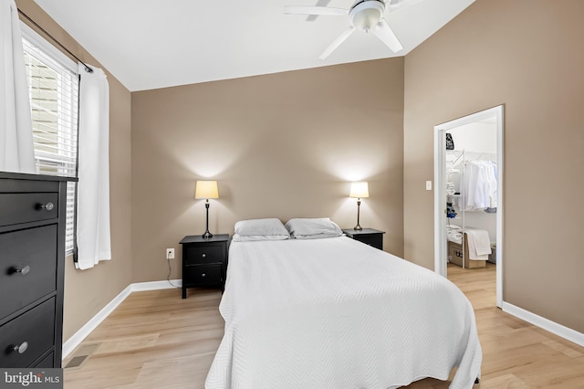 bedroom with ceiling fan, a walk in closet, light hardwood / wood-style floors, and vaulted ceiling