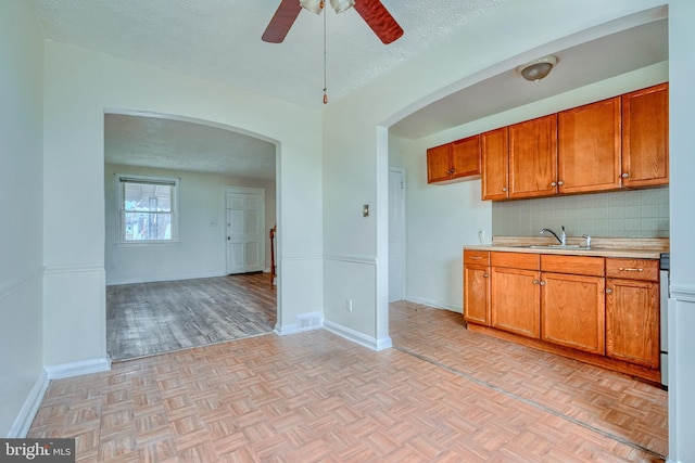 kitchen with sink, a textured ceiling, ceiling fan, light parquet flooring, and decorative backsplash