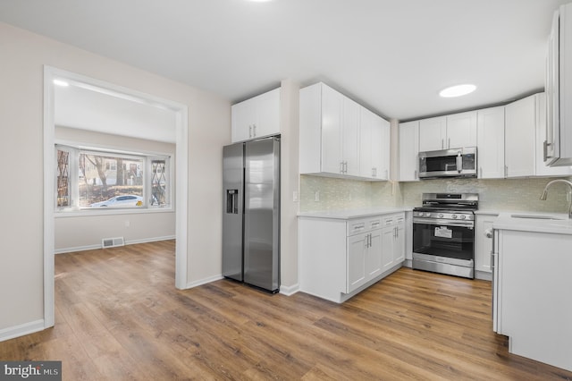 kitchen with white cabinetry, sink, decorative backsplash, light hardwood / wood-style floors, and stainless steel appliances