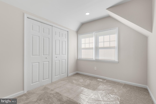 unfurnished bedroom featuring lofted ceiling, light carpet, and a closet