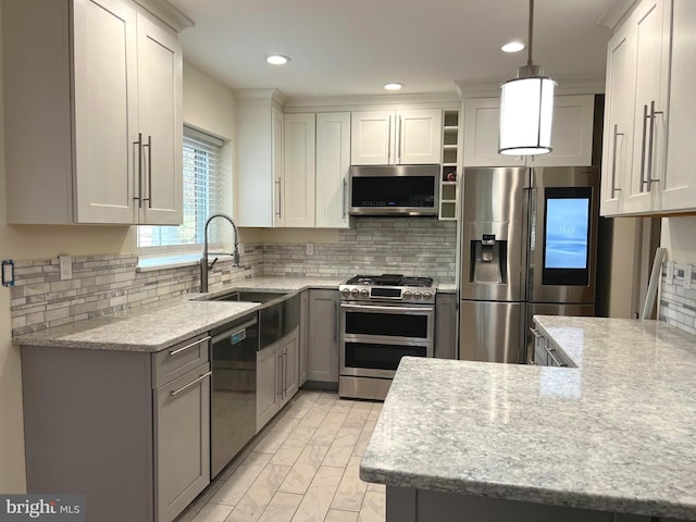 kitchen featuring light stone counters, stainless steel appliances, a sink, and decorative light fixtures