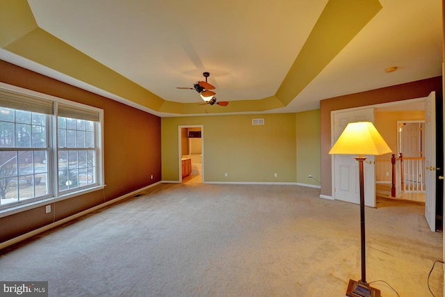 interior space with a raised ceiling, light colored carpet, and ceiling fan