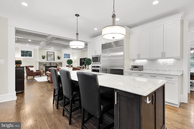 kitchen featuring white cabinets, dark hardwood / wood-style flooring, hanging light fixtures, built in appliances, and a center island with sink