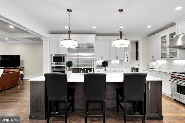 kitchen with hanging light fixtures, a kitchen island with sink, built in appliances, and white cabinets