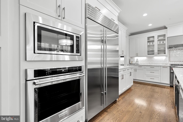 kitchen with dark hardwood / wood-style floors, white cabinets, backsplash, built in appliances, and light stone countertops