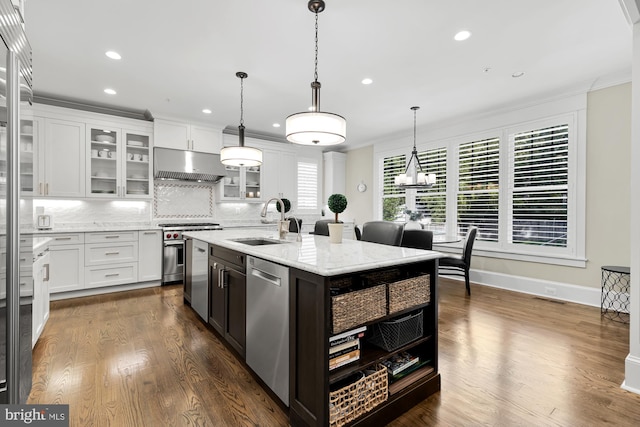 kitchen with appliances with stainless steel finishes, ventilation hood, white cabinetry, sink, and a center island with sink