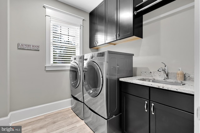 clothes washing area featuring cabinets, washer and clothes dryer, sink, and light wood-type flooring