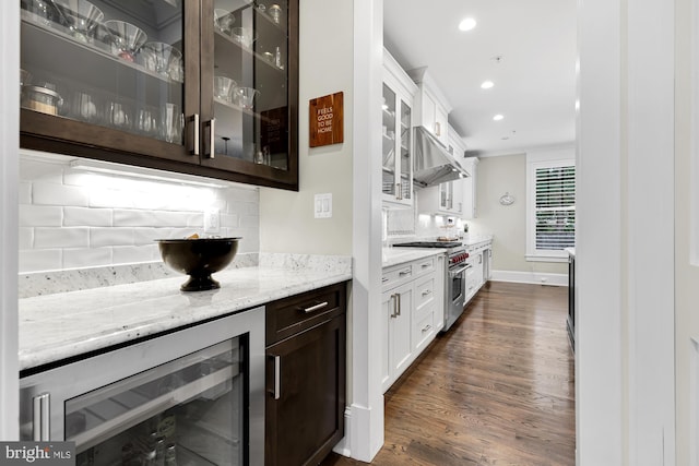 kitchen featuring high end stainless steel range, light stone counters, white cabinets, beverage cooler, and backsplash