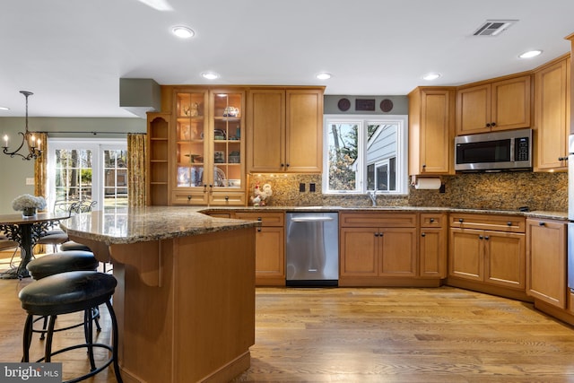 kitchen with a breakfast bar area, hanging light fixtures, light wood-type flooring, stone counters, and stainless steel appliances