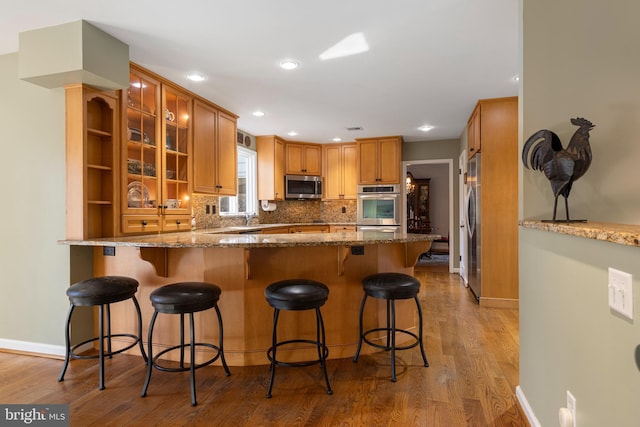 kitchen with tasteful backsplash, light hardwood / wood-style flooring, kitchen peninsula, stone counters, and stainless steel appliances