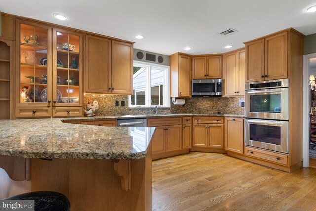 kitchen with a kitchen bar, light stone counters, kitchen peninsula, stainless steel appliances, and light hardwood / wood-style floors