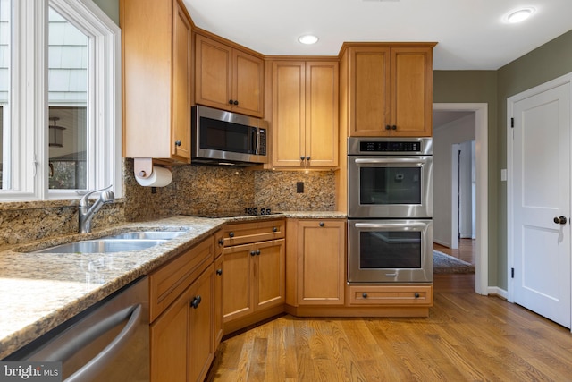 kitchen with light stone counters, sink, light wood-type flooring, and appliances with stainless steel finishes